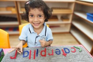 Smiling young child in a classroom sitting at a table with colorful magnetic letters