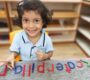 Smiling young child in a classroom sitting at a table with colorful magnetic letters Starshine Montessori 90x80