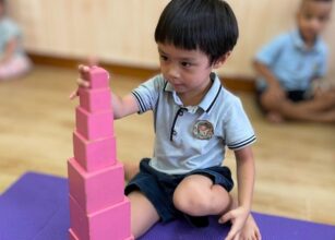 A child carefully stacking pink blocks on a purple mat in a classroom