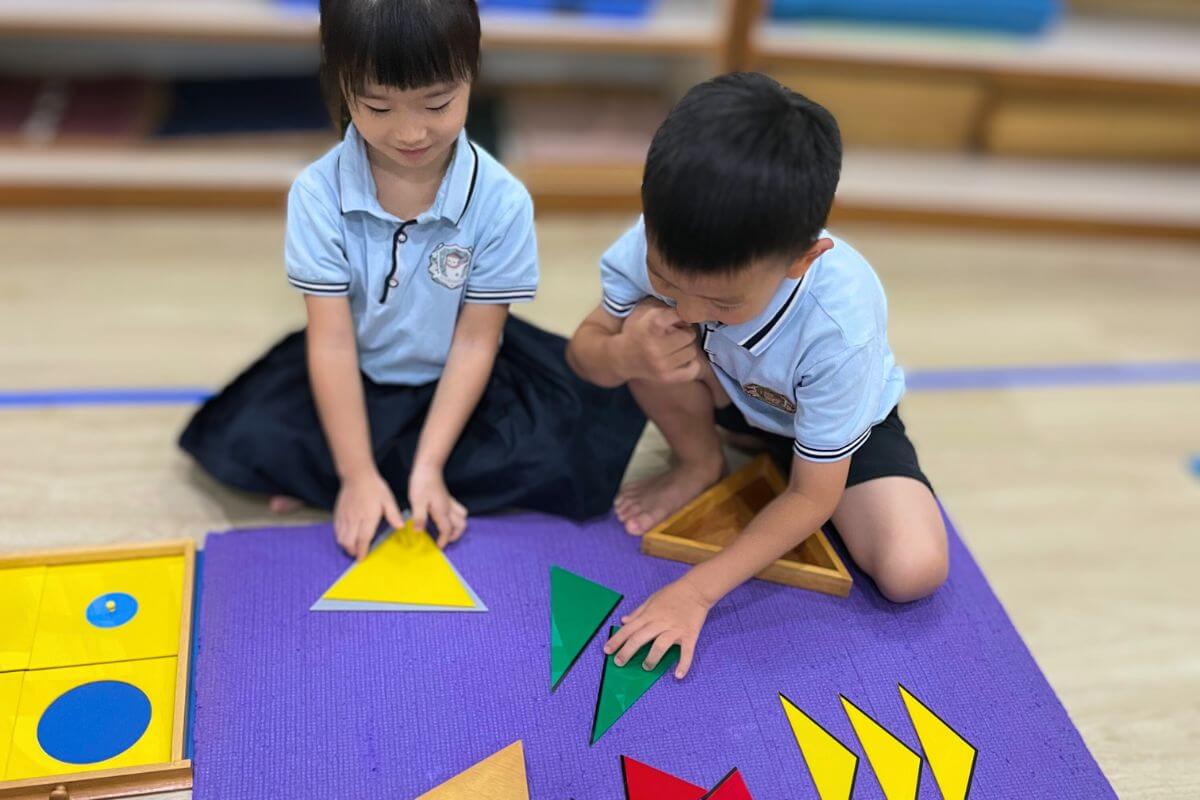 Children in uniforms play with shape puzzles on a purple mat in a classroom
