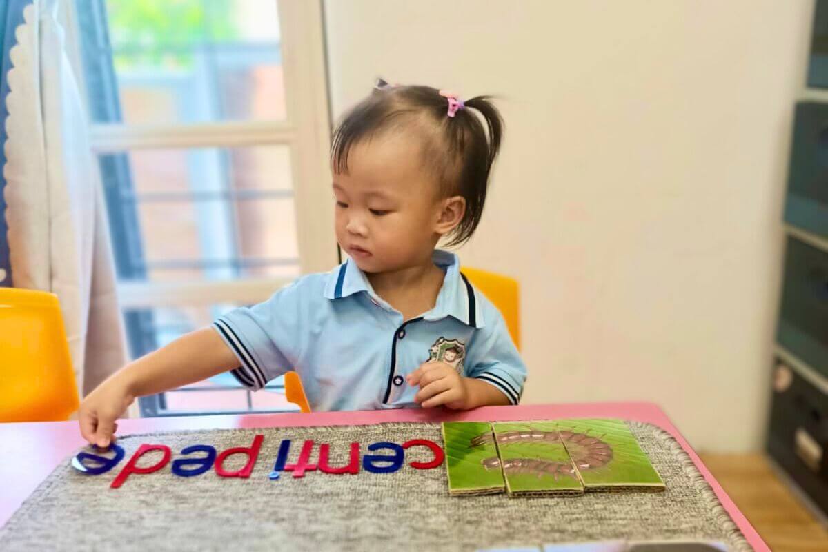 Preschool girl with hair tied up playing with colorful letter magnets on a table in a classroom setting