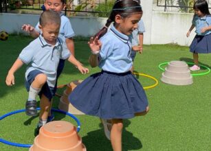 Preschoolers in uniforms playing with hoops and cones on green turf at Starshine Montessori, showcasing outdoor learning activities