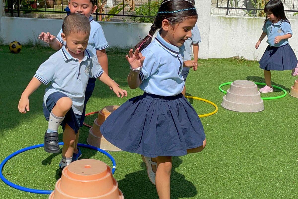 Preschoolers in uniforms playing with hoops and cones on green turf at Starshine Montessori, showcasing outdoor learning activities