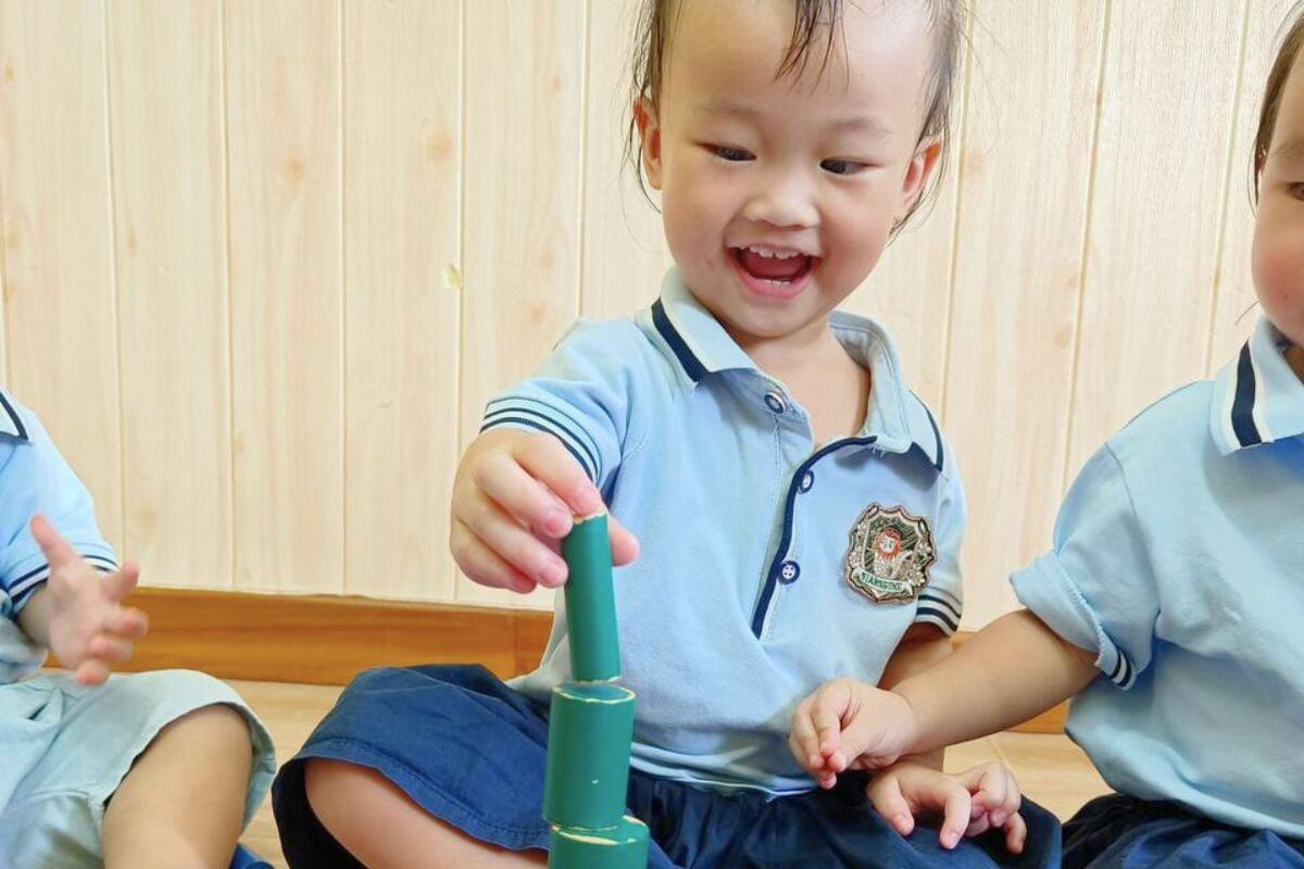 Smiling toddler stacking green blocks in school uniform, indoor playtime activity