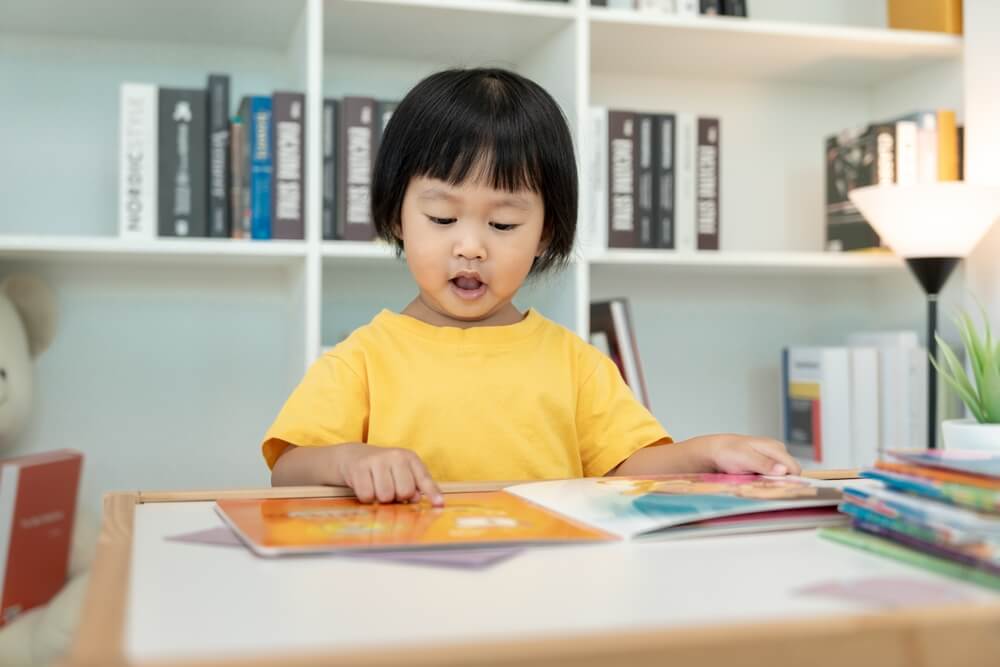 Child reading a book, engaging in early literacy development and learning in classroom environment.