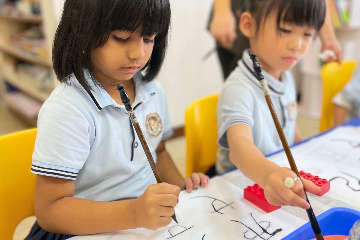 Young children practising Chinese calligraphy during a classroom activity in a Singapore preschool, fostering cultural learning and fine motor skills.