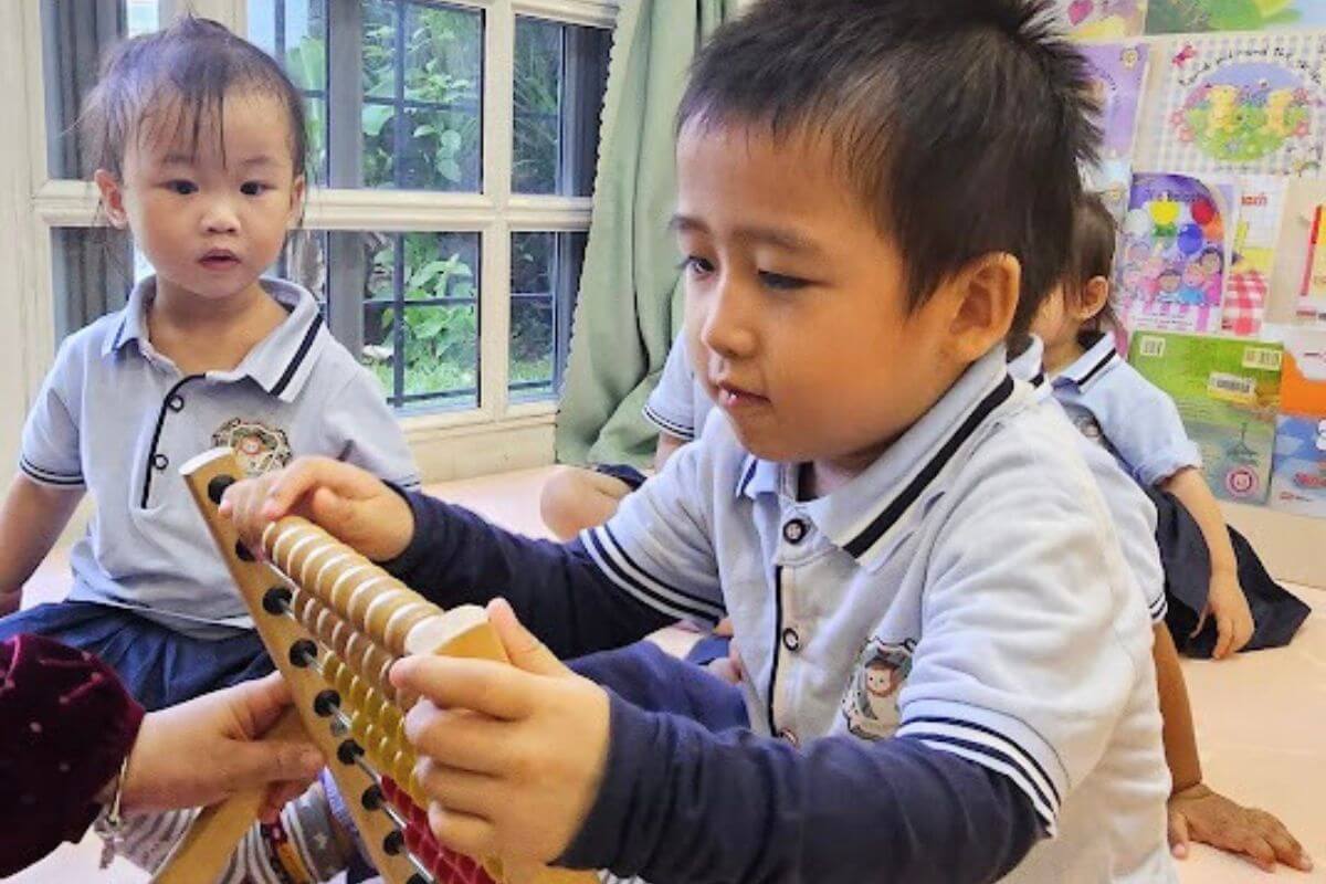 A young boy engaging with a colorful wooden abacus, with other children observing and a bright classroom environment at Starshine Montessori.