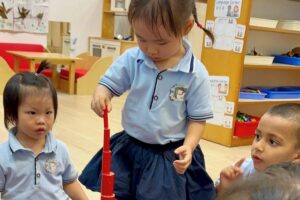 Young children in a classroom stacking red blocks while sitting together and focusing on the Montessori activity at Starshine Montessori.