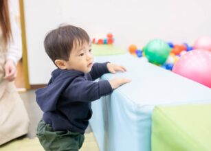 Toddler learning to stand and explore during playtime, developing gross motor skills through movement and physical activity.