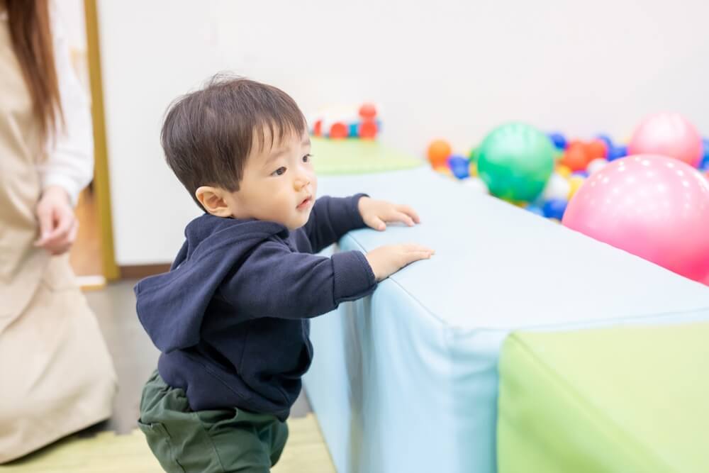 Toddler learning to stand and explore during playtime, developing gross motor skills through movement and physical activity.