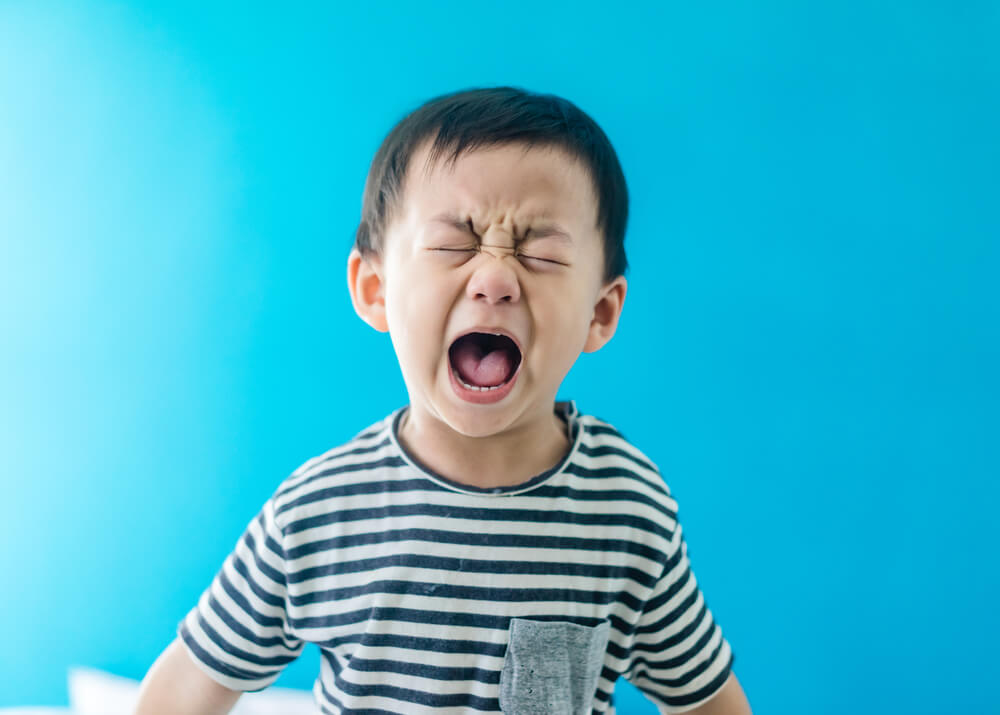 A young child crying with an emotional expression, wearing a striped shirt against a blue background, depicting childhood emotions and communication.