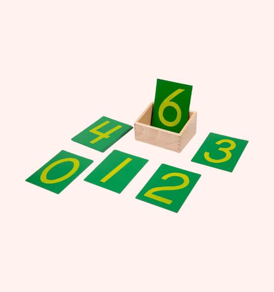 Montessori sandpaper numbers displayed in green cards with yellow numerals, arranged neatly alongside a wooden storage box.