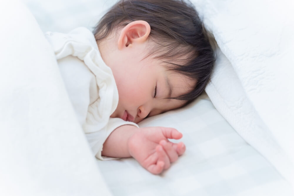 A peaceful baby sleeping soundly on a soft white bed, partially covered with a blanket.