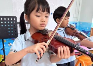 A young girl attentively playing the violin during a music lesson, demonstrating focus and precision. A boy in the background is also playing the violin, emphasising collaborative learning in a classroom at Starshine Montessori.