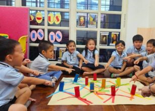 A group of young children sitting in a circle on the floor, participating in a Montessori group activity with colorful paper tubes and ribbons, engaging in a hands-on learning experience at Starshine Montessori.