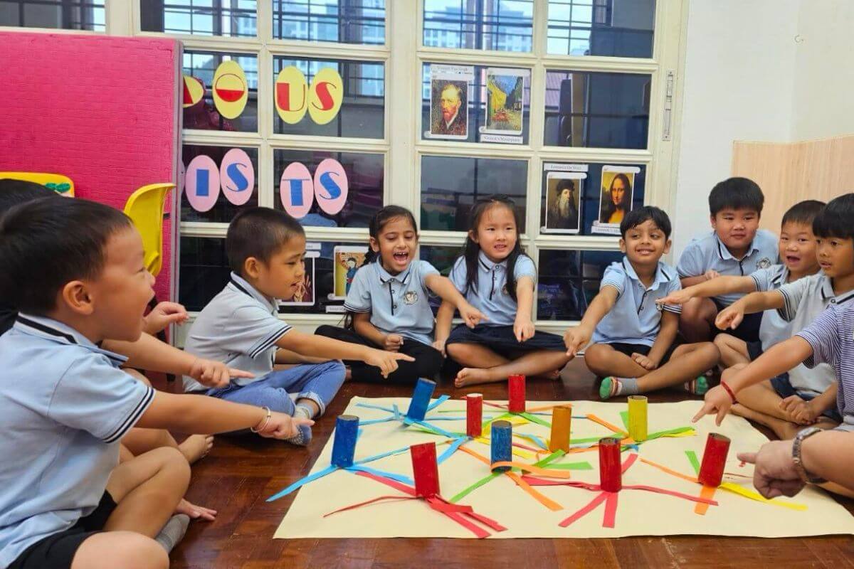 A group of young children sitting in a circle on the floor, participating in a Montessori group activity with colorful paper tubes and ribbons, engaging in a hands-on learning experience at Starshine Montessori.