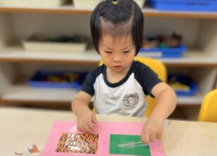 A young child in a Montessori classroom is engaged in a texture matching activity. The child is carefully placing a transparent card on a pink sensory board featuring different textured and patterned squares, reinforcing tactile learning and sensory exploration at Starshine Montessori.