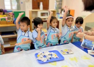 Young children in a Montessori classroom at Starshine Montessori preschool participating in an interactive art painting activity, wearing aprons and engaging with their teacher. The learning environment encourages creativity, self-expression, and hands-on exploration through guided artistic experiences.