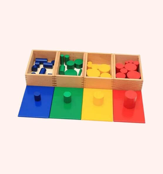 Montessori knobbed cylinder blocks color set – A hands-on educational material designed to develop fine motor skills, shape and size differentiation, and problem-solving abilities in young children. Features red, yellow, green, and blue wooden cylinders with matching baseboards.