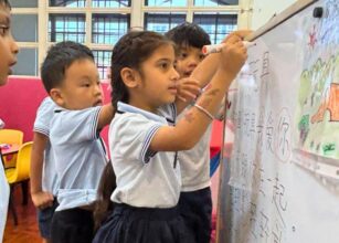 Group of young children participating in a collaborative whiteboard activity in a Montessori classroom at Starshine Montessori Preschool. The students are writing and drawing on the board, practicing language skills and creative expression, fostering teamwork and hands-on learning.