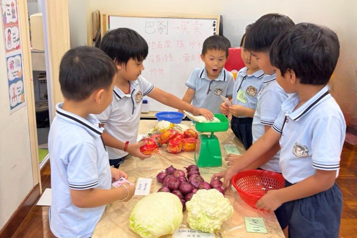 Young children engaged in a Montessori classroom market role-play activity, using real vegetables, a weighing scale, and shopping baskets. This hands-on learning experience promotes practical life skills, teamwork, and early math concepts in a fun and interactive environment at Starshine Montessori preschool.